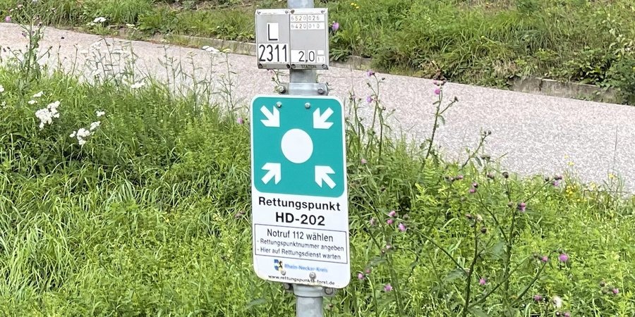 Schild als Hinweis auf einen Rettungspunkt an einem Weg an einer Wiese.